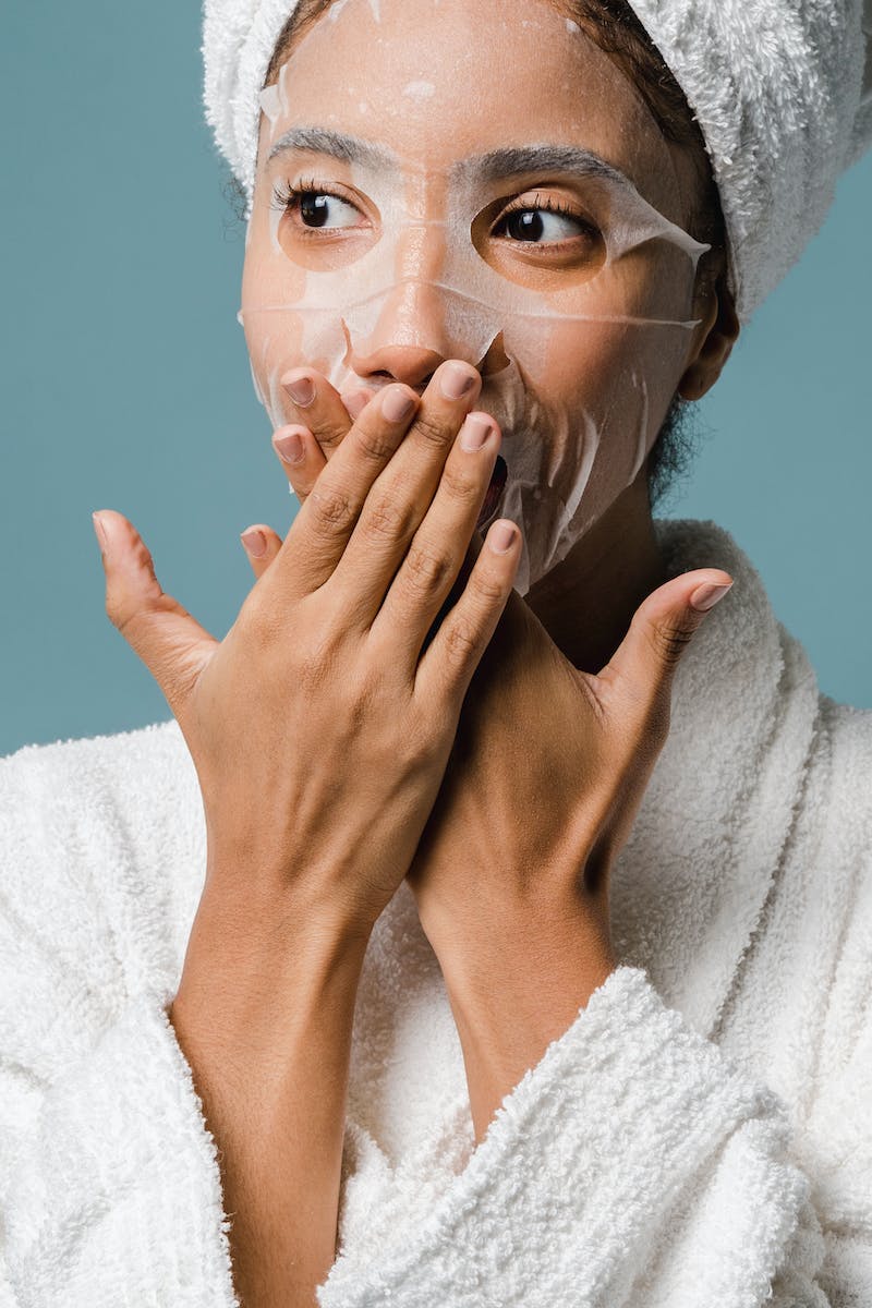 Amazed young ethnic woman covering mouth with hands during skin care routine